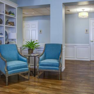 A cozy living room with blue chairs, a small table with a plant, and hardwood floors.