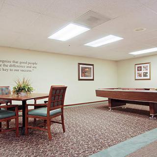 A recreational room featuring a pool table and a small table with chairs, accented by wall art and carpet flooring.