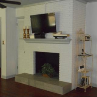 A modern living room features a flat-screen TV mounted above a fireplace, complemented by decorative items and a corner shelf.