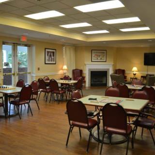 A spacious community dining room with tables and chairs arranged neatly, featuring a cozy fireplace.