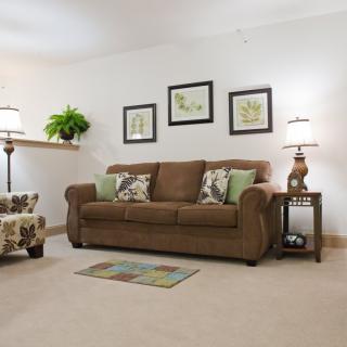 A cozy living room with a brown sofa, decorative pillows, artwork on the wall, and warm ambient lighting.