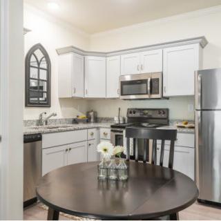 A modern kitchen with white cabinetry, stainless steel appliances, and a small dining table with a flower centerpiece.