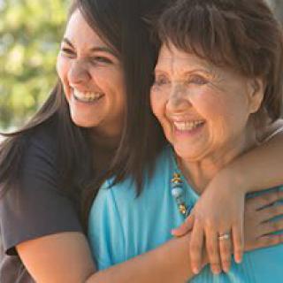 A warm embrace between two smiling women outdoors.