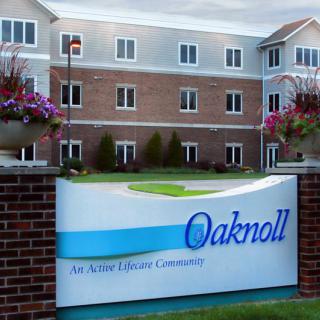 Sign for Oaknoll, an active retirement community, in front of a large brick building.