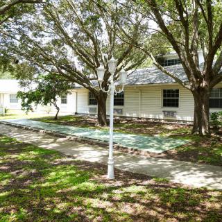 A peaceful outdoor scene featuring a house surrounded by trees, with a lamp post and benches along a pathway.