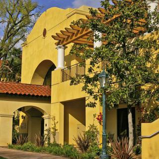A Mediterranean-style building with a yellow facade surrounded by trees on a sunny day.