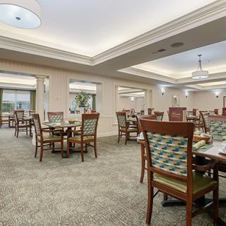 A spacious and elegantly decorated dining room with multiple tables and chairs, featuring a carpeted floor and ambient lighting.