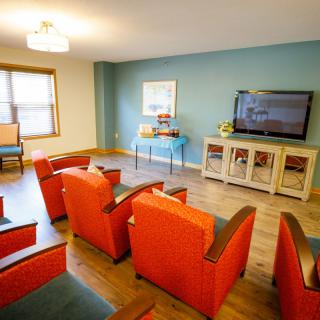 A vibrant living room with orange chairs and a wall-mounted TV.