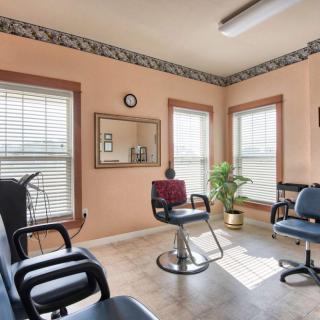 An empty hair salon with multiple chairs, a mirror, and large windows letting in natural light.
