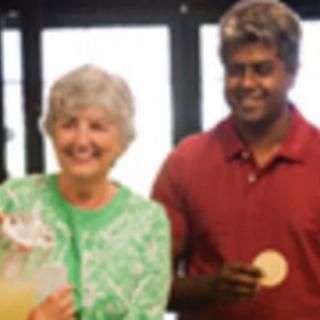 Two people smiling indoors, one holding a beverage and the other holding a cookie.