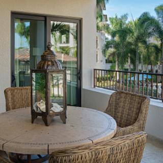 A serene balcony setting with wicker furniture and a decorative lantern, surrounded by lush palm trees.
