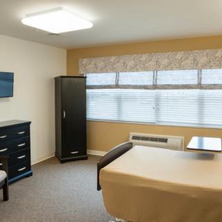 A well-lit room with a bed, dresser, wardrobe, and a wall-mounted TV.