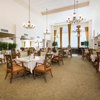 An elegant restaurant dining room with neatly arranged tables and chairs, adorned with chandeliers and large windows.