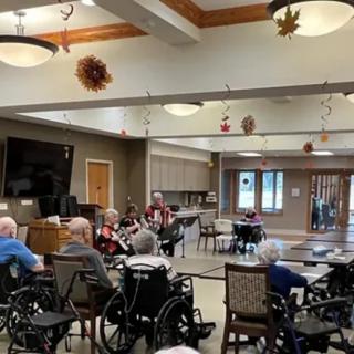 A community room in a nursing home with elderly residents gathering, some using wheelchairs.