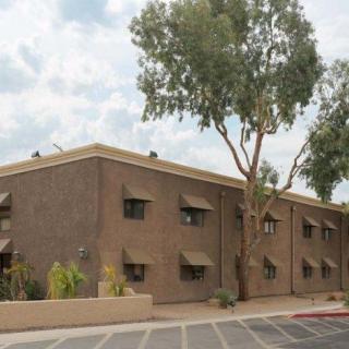 A residential apartment building with trees in front and a cloudy sky backdrop.