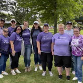 A group of people wearing purple shirts gathered outdoors in a park setting.