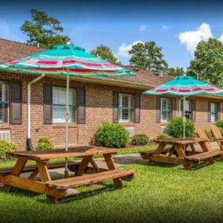 Outdoor picnic area with wooden tables and umbrellas in front of a brick building on a sunny day.