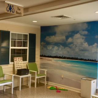 A waiting area with green chairs and a beach mural on the wall.