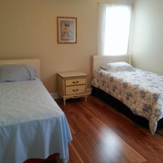 A minimalist bedroom featuring two single beds, a nightstand, and a window with natural light.