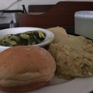 A hearty meal featuring a bread roll, cooked greens, and a grain dish.
