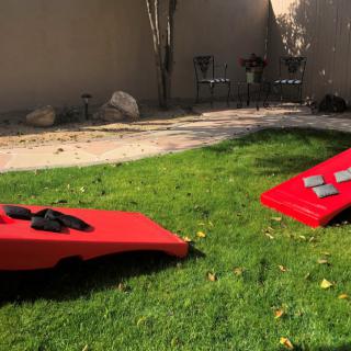 Two red cornhole boards set up on a grassy backyard for an outdoor game.