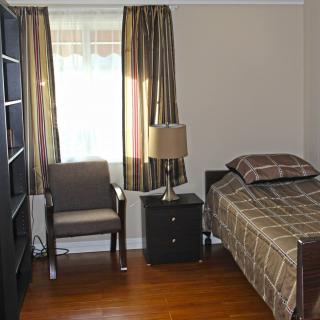 A cozy bedroom with a single bed, nightstand, chair, and bookshelf by the window.