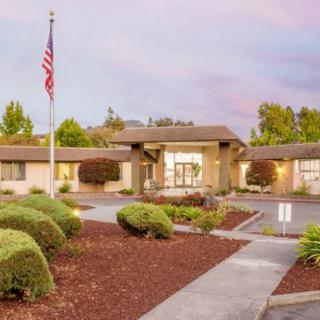 A serene view of a building with an American flag, surrounded by well-maintained landscaping and a clear sky.