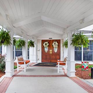 A welcoming porch with hanging plants and decorated double front doors.