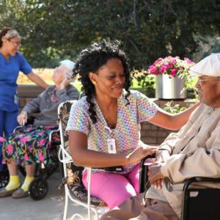 Healthcare workers interacting with elderly individuals outdoors in a caring environment.