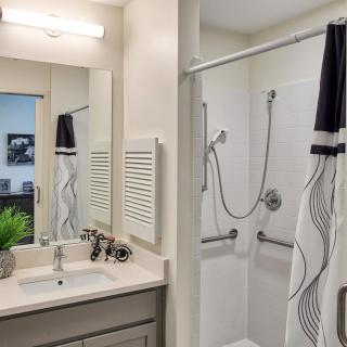 A modern bathroom with a sink and mirror next to a shower area with patterned curtains.