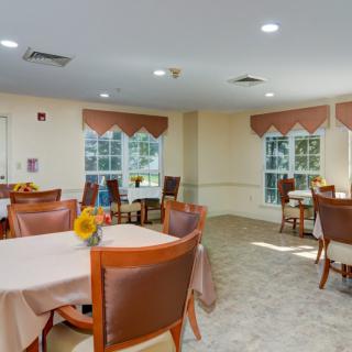 A well-lit dining area with tables and chairs, decorated with sunflowers near large windows.