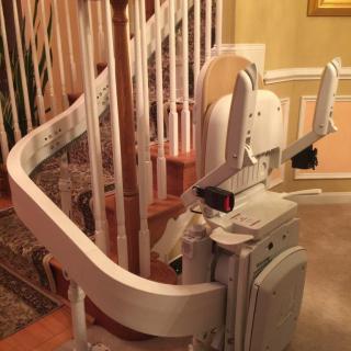 A stairlift installed along a curved staircase in a home, designed for accessibility and mobility assistance.