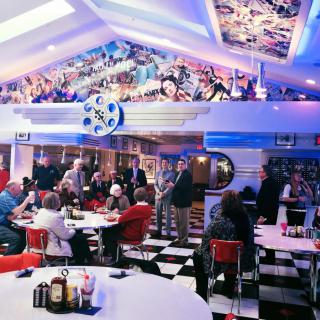 A bustling retro diner with a colorful decor and a checkerboard floor, filled with people enjoying their meals.