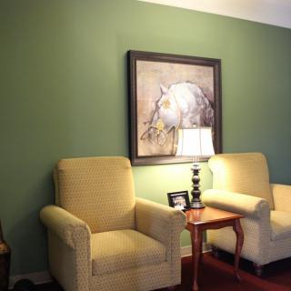 A cozy living room setup with two armchairs, a side table with a lamp, and artwork on a green wall.