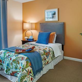 A cozy bedroom with a single bed featuring colorful bedding, an orange accent wall, and a stylish lamp on the side table.