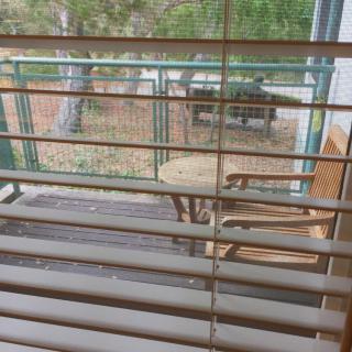 A view of outdoor furniture through window blinds, featuring a wooden deck with chairs and a table.