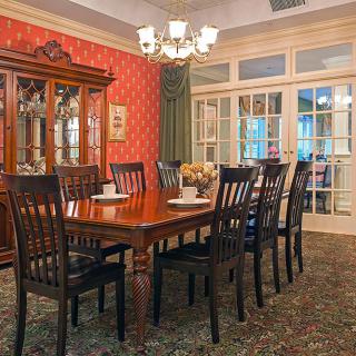 A traditional dining room with a large wooden table and chairs, a chandelier overhead, and a china cabinet against the red wallpapered wall.