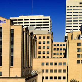 A cityscape featuring a large hospital complex with tan buildings against a clear blue sky.