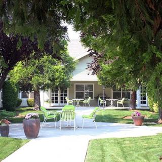 A cozy house surrounded by lush gardens and trees, featuring outdoor patio furniture on the lawn.