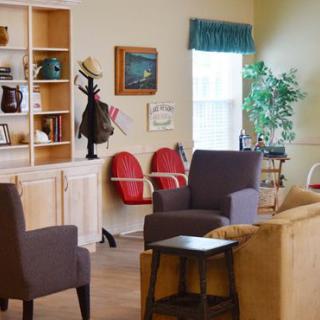 A cozy living room with chairs, a sofa, and a well-decorated bookshelf.