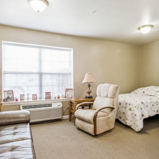 A cozy bedroom with a bed, armchair, and a window providing natural light.