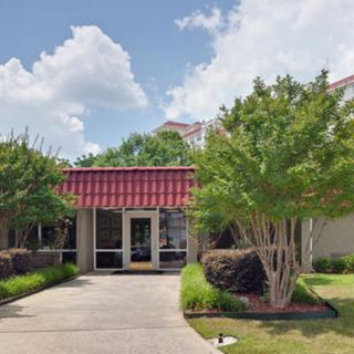 The entrance of a building with a red roof, surrounded by trees and landscaping under a cloudy sky.
