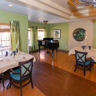 A cozy dining room with a grand piano, featuring elegant tables and chairs on a wooden floor.