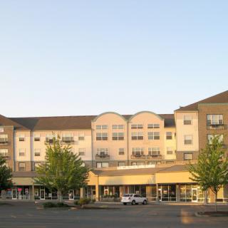 A shopping center building with a parking lot in front, surrounded by trees.