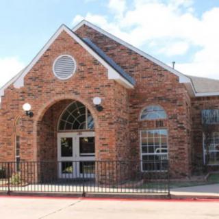 A brick building with arched windows and a gated entrance under a clear sky.