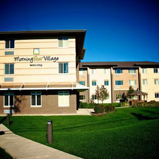 A modern apartment building with a well-maintained lawn and clear blue sky.