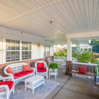 A cozy porch with wicker furniture and red cushions, perfect for relaxing outdoors.