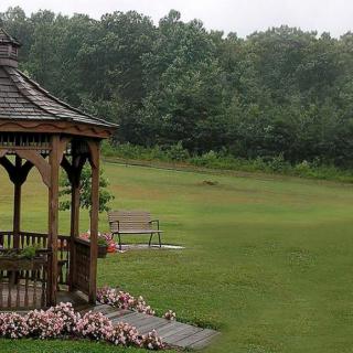 A peaceful park scene with a wooden gazebo surrounded by flowers and a bench overlooking the lush greenery.