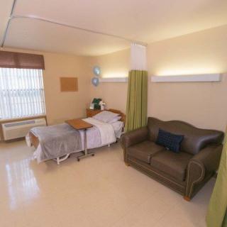 A clean and organized hospital room featuring a bed, a couch, and light-colored curtains.