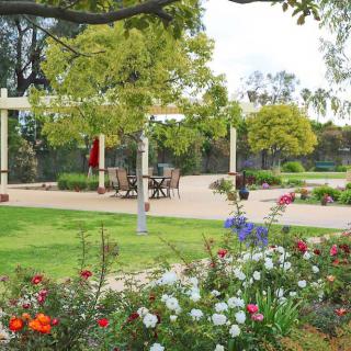A beautifully landscaped garden with colorful flowers and a patio seating area surrounded by trees.